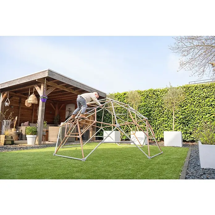 Exit Toys Klettergerüst Climbing Dome - Ø x H: 300 x 165 cm, Stahl, Pastell - Kind klettert auf ein zweifarbiges (grau und kupferfarbenes) Geodätisches Klettergerüst im Garten.