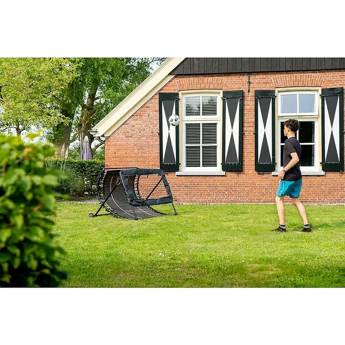 Exit Toys Fußballtor Kickback Rebounder - 142 x 105 cm, Schwarz - Schwarzes Fußball-Reboundernetz in einem grünen Garten, von einer Person zum Training genutzt.