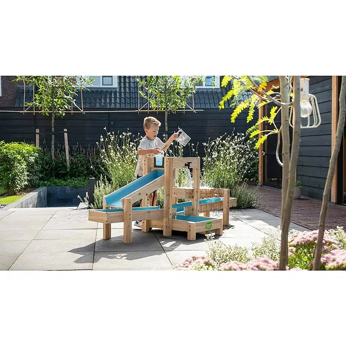 Exit Toys Wasserbahn Aquaflow - Holz, Natur/Blau, 221 x 73 x 90 cm - Ein kleiner Junge spielt mit einem hölzernen Wasserspieltisch mit blauen Elementen in einem Garten.