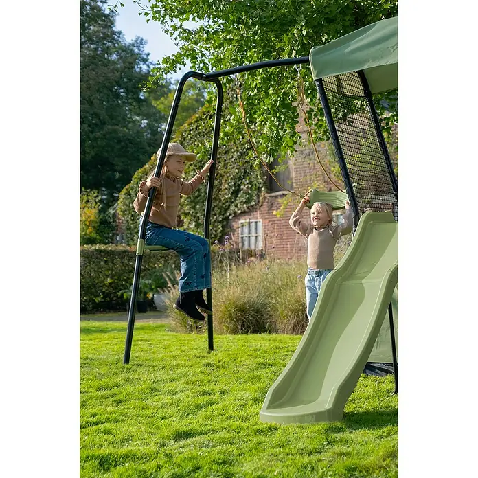 Exit Toys Spielhaus Ivy - L x B x H: 253 x 268 x 216 cm, Holz, Grün/Schwarz, Mit Rutsche und Schaukel - Zwei Kinder spielen im Garten auf einer schwarz-grünen Schaukel mit Rutsche. Das Set hat zwei Schaukeln und eine kleine Rutsche.