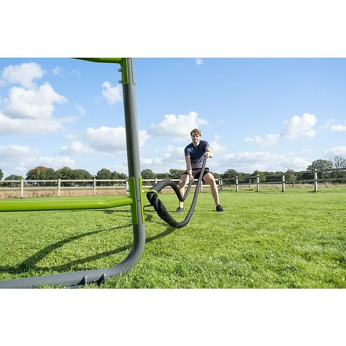 Exit Toys Klettergerüst GetSet Battle Rope-Ringe - 2 Stk., Passend für: Alle GetSet Monkeybars und Powerstations, Schwarz - Mann trainiert mit einem schwarzen Battle Rope, das an einem grünen und grauen Outdoor-Fitnessrahmen auf Gras befestigt ist.