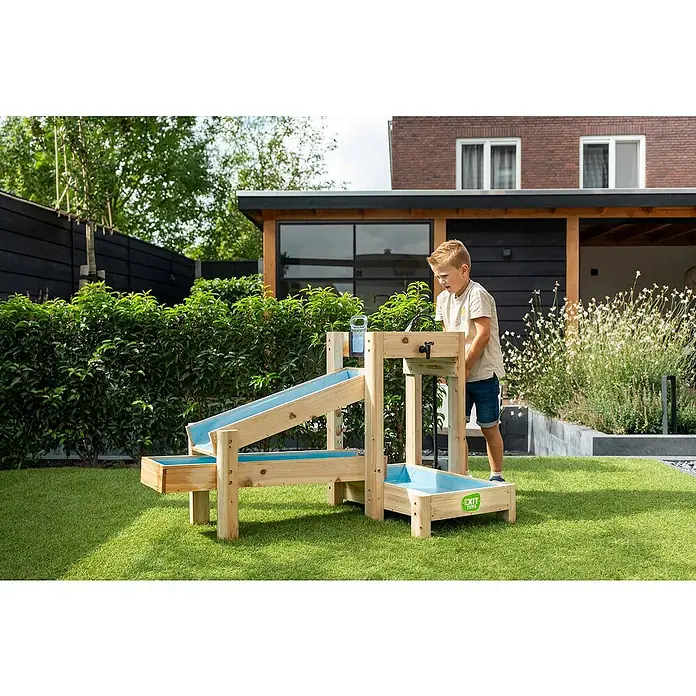 Exit Toys Wasserbahn Aquaflow - Holz, Natur/Blau, 140 x 73 x 90 cm - Ein Kind spielt mit einem hölzernen Wasserspieltisch mit blauen Kanälen und einem Wasserhahn im Garten.