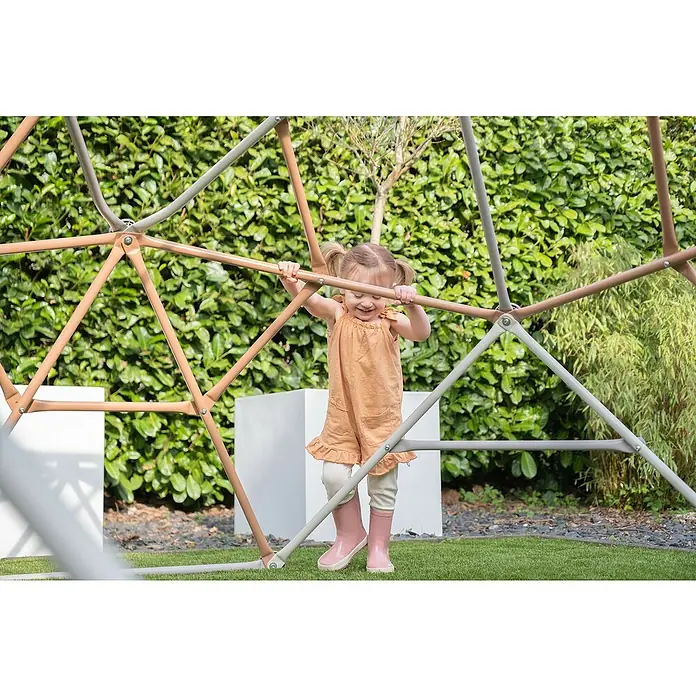 Exit Toys Klettergerüst Climbing Dome - Ø x H: 300 x 165 cm, Stahl, Pastell - Ein glückliches Kind spielt auf einer zweifarbigen Metall-Kletterkuppel im Garten.