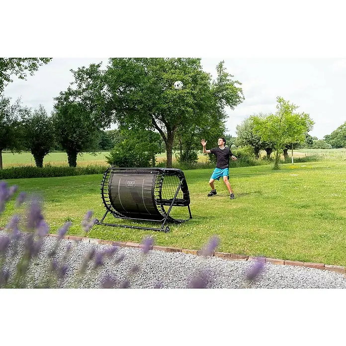 Exit Toys Fußballtor Kickback Rebounder - 142 x 105 cm, Schwarz - Schwarzer Fußball-Rebounder auf Gras, von einer Person zum Balltraining mit einem Fußball im Park genutzt.