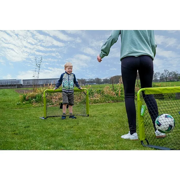 Exit Toys Fußballtor Tempo 900 Mini - 2 Stk., B x H: 90 x 60 cm, Grün/Schwarz - Zwei grüne Mini-Fußballtore auf einem Feld, eines mit einem Kind, ein anderes mit einem Erwachsenen und einem Ball, bereit zum Spielen.