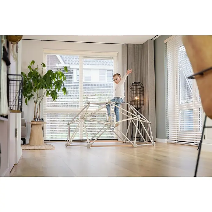 Exit Toys Klettergerüst Climbing Dome - Ø x H: 190 x 92 cm, Stahl, Pastell - Ein kleiner Junge spielt aktiv auf einem hellen, geometrischen Klettergerüst für drinnen.