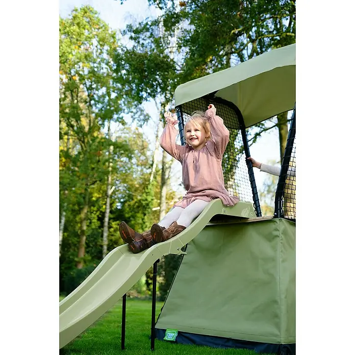 Exit Toys Spielhaus Ivy - L x B x H: 253 x 135 x 216 cm, Holz, Grün/Schwarz, Mit Rutsche - Ein lächelndes Kind rutscht eine grüne Spielturm-Rutsche hinunter, genießt den Spaß im Freien.
