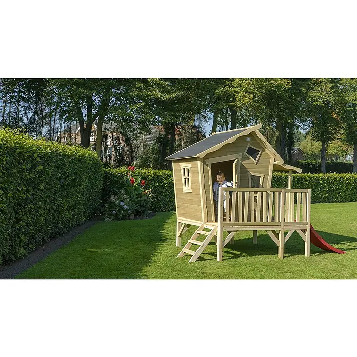 Exit Toys Spielhaus Crooky 350 - L x B x H: 322 x 184 x 227 cm, Holz, Grau/Beige - Erhöhtes Holzspielhaus mit Treppe, roter Rutsche und einem Kind, das herausschaut, in einem sonnigen Garten.