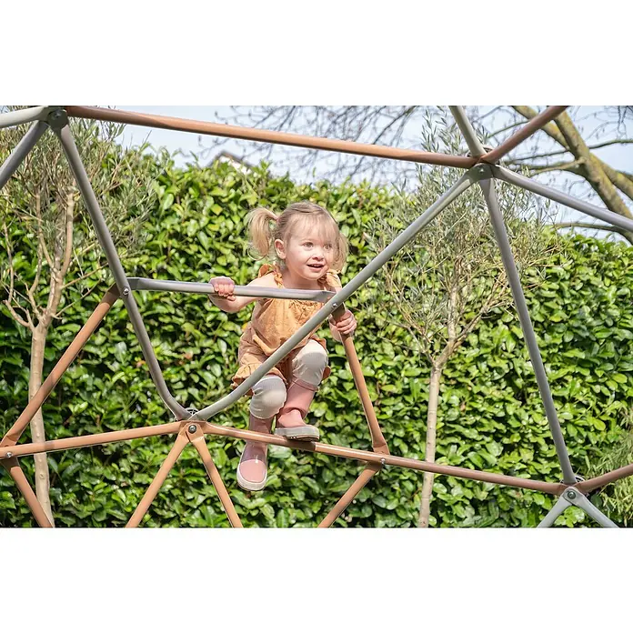 Exit Toys Klettergerüst Climbing Dome - Ø x H: 300 x 165 cm, Stahl, Pastell - Ein Kind klettert auf einem geometrischen Klettergerüst mit braunen und grauen Metallrohren, draußen im Garten.