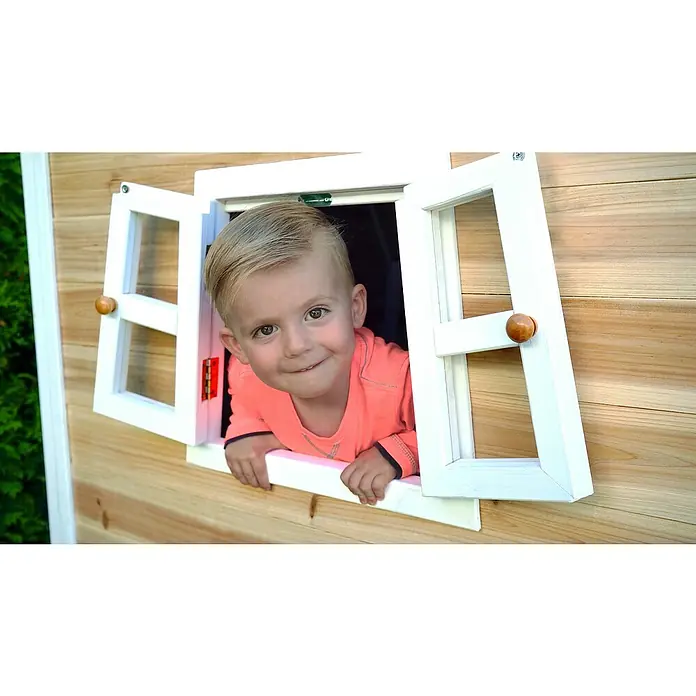 Exit Toys Spielhaus Fantasia 100 - L x B x H: 128 x 108 x 171 cm, Holz, Natur - Lächelndes Kind schaut aus einem Naturholz-Spielhaus mit weiß gerahmten Fenstern.