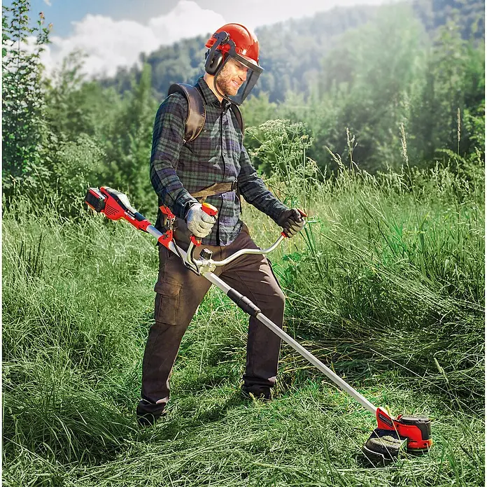 Einhell PXC 18V Desbrozadora de batería Agillo 36/255 - 36 V, 4 Ah, 2 baterías - Hombre con equipo de protección usa una desbrozadora roja y negra para cortar hierba alta.