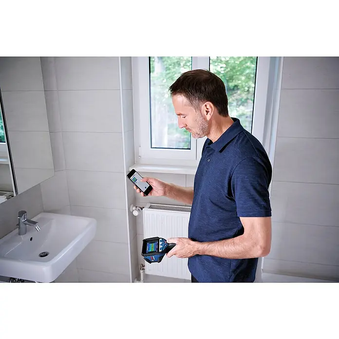 Bosch Professional Wärmebildkamera GTC 600 C PRO - Messbereich Temperatur: -20 °C - 600 °C - Ein Mann inspiziert ein Badezimmer mit einer blau-schwarzen Wärmebildkamera, verbunden mit einem Smartphone, das Wärmewerte anzeigt.