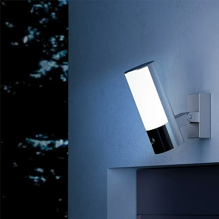 EZVIZ Überwachungskamera EL3 2560 × 1440 mit Beleuchtung - Weiß, Erfassungsreichweite: 15 m - Moderne silberne Wandleuchte mit schwarzem Sockel, weißes Licht ausstrahlend, nachts an einer blauen Wand montiert.