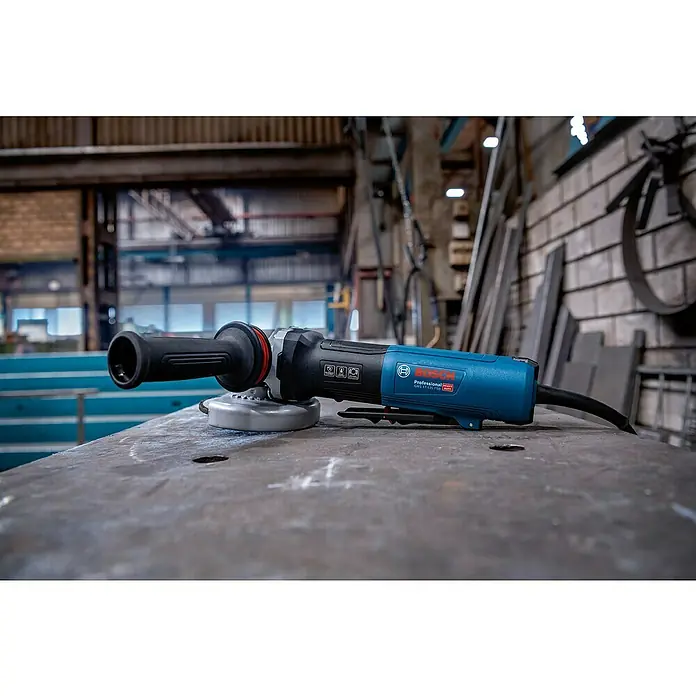 Bosch Professional Elektro-Winkelschleifer GWS 17-125 PSB - 1.700 W, Durchmesser Scheibe: 125 mm, Leerlaufdrehzahl: 2.800 U/min - 11.500 U/min - Blau-schwarzer Bosch Professional Winkelschleifer mit Griff und Netzkabel auf einer Metallwerkbank in einer Werkstatt.