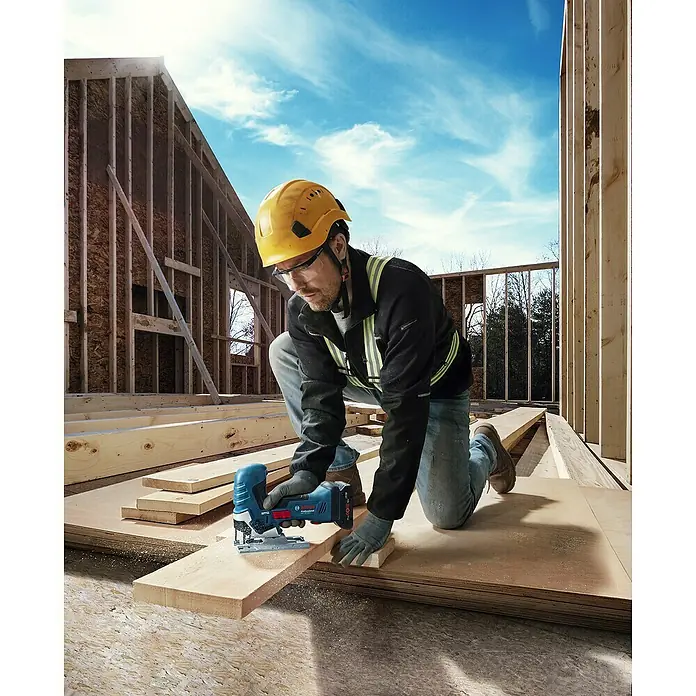 Bosch Professional AMPShare 18V Akku-Stichsäge GST 18V-125 S PRO SOLO - 18 V, Ohne Akku, 500 /min - 3.500 /min - Ein Bauarbeiter schneidet mit einer blauen Bosch Akku-Stichsäge ein Holzbrett auf einer Baustelle.