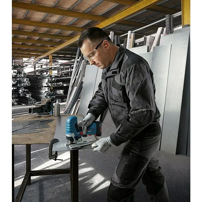 Bosch Professional AMPShare 18V Akku-Stichsäge GST 18V-125 S PRO SOLO - 18 V, Ohne Akku, 500 /min - 3.500 /min - Ein Arbeiter in Schutzkleidung benutzt eine blau-schwarze Bosch Akku-Stichsäge, um ein Metallblech auf einer Werkbank zu schneiden.