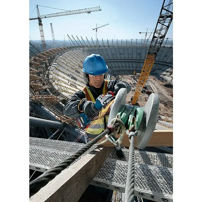 Bosch Professional AMPShare 18V Akku-Winkelschleifer GWS 18V-10 P PRO - 2 Akkus, Durchmesser Scheibe: 125 mm - Arbeiter nutzt einen blauen Bosch 18V Akku-Winkelschleifer, erzeugt Funken beim Schneiden von Metall auf einer hohen Baustelle.