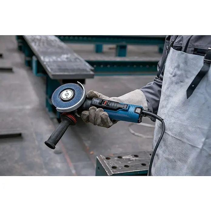 Bosch Professional Elektro-Winkelschleifer GWS 17-125 PSB - 1.700 W, Durchmesser Scheibe: 125 mm, Leerlaufdrehzahl: 2.800 U/min - 11.500 U/min - Eine Person in Schutzkleidung hält einen blauen Winkelschleifer mit einer grauen Schleifscheibe in einer Werkstatt.
