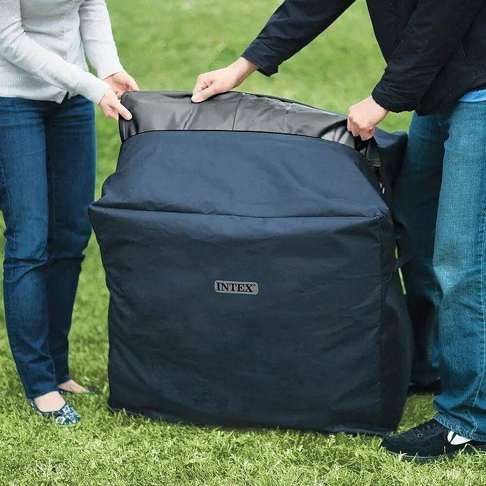 Intex Pure Spa Hidromasaje móvil Greenwood - Ø x Al: 216 x 71 cm, Gris/Blanco, 1.098 l - Dos personas manipulan una bolsa grande de tela Intex de color azul oscuro, probablemente para almacenar o transportar.