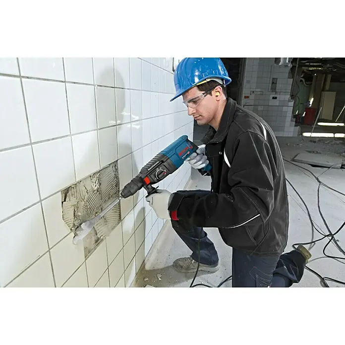 Bosch Professional Bohrhammer-Set GBH 2-26 F - 2,7 J - Mann in Schutzausrüstung verwendet einen blauen Bosch Bohrhammer, um weiße Fliesen von einer Wand zu entfernen.