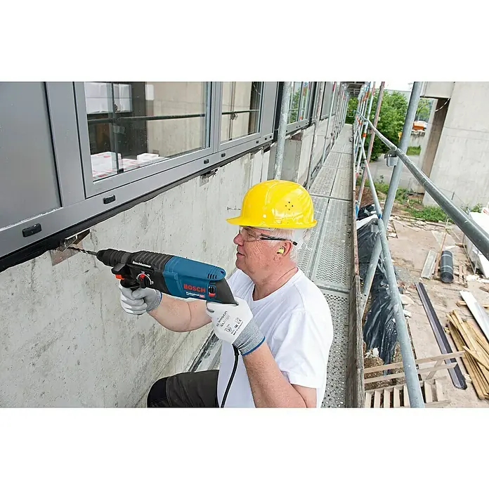 Bosch Professional Bohrhammer-Set GBH 2-26 F - 2,7 J - Ein Mann bohrt mit einem blau-schwarzen Boschhammer-Bohrhammer in eine Betonwand auf einer Baustelle.