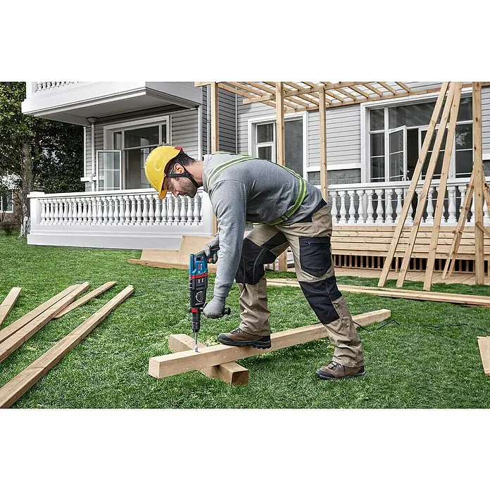 Bosch Professional Bohrhammer-Set GBH 2-26 F - 2,7 J - Mann in Arbeitskleidung bohrt mit einem blau-roten Bohrhammer in einen Holzbalken im Freien.