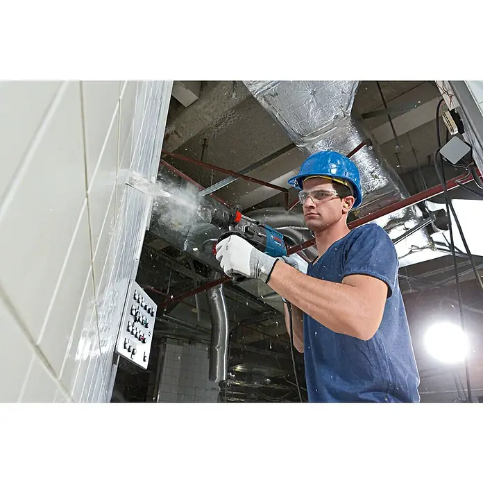 Bosch Professional Bohrhammer GBH 2-28 F - 880 W, 3,2 J, SDS-Plus-Aufnahme - Mann in Schutzausrüstung verwendet einen blau-schwarzen Bohrhammer, um eine weiße Fliesenwand zu durchbrechen, Staub erzeugend.