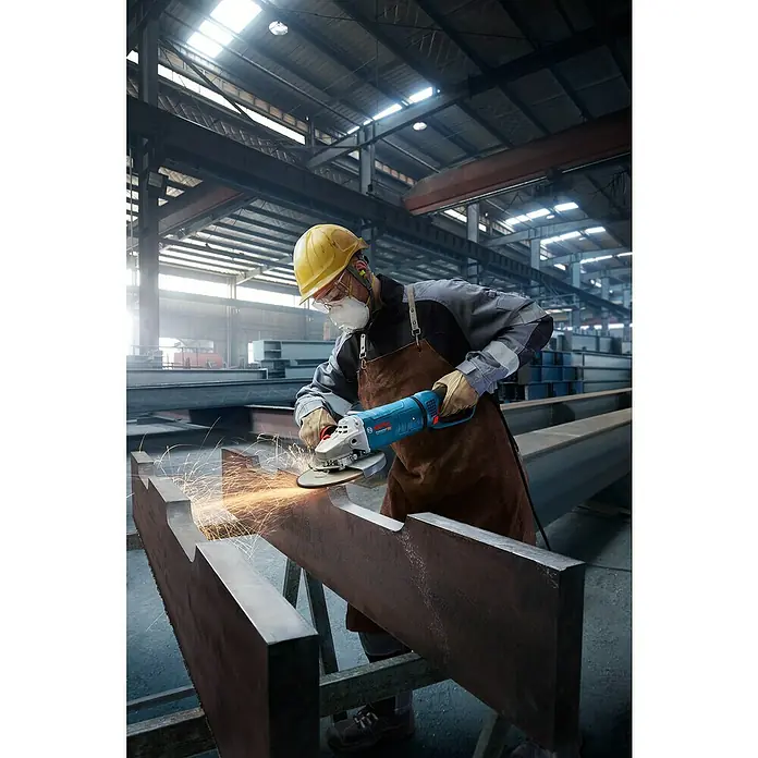 Bosch Professional Elektro-Winkelschleifer GWS 27-230 JR - 2.700 W, Durchmesser Scheibe: 230 mm, Leerlaufdrehzahl: 5.200 U/min - 6.500 U/min - Arbeiter benutzt einen blau-silbernen Winkelschleifer an einem Metallbalken in einer Fabrik, Funken erzeugend.