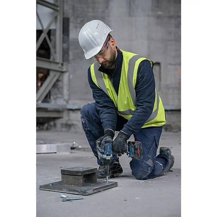 Bosch Professional AMPShare 18V Akku-Drehschlagschrauber GDS 18V-750 C - 18 V, Ohne Akku - Blauer und schwarzer Bosch Akku-Schlagschrauber mit ProCORE 18V Akku, von einem Arbeiter zum Befestigen einer Schraube in einer Metallbasis verwendet.