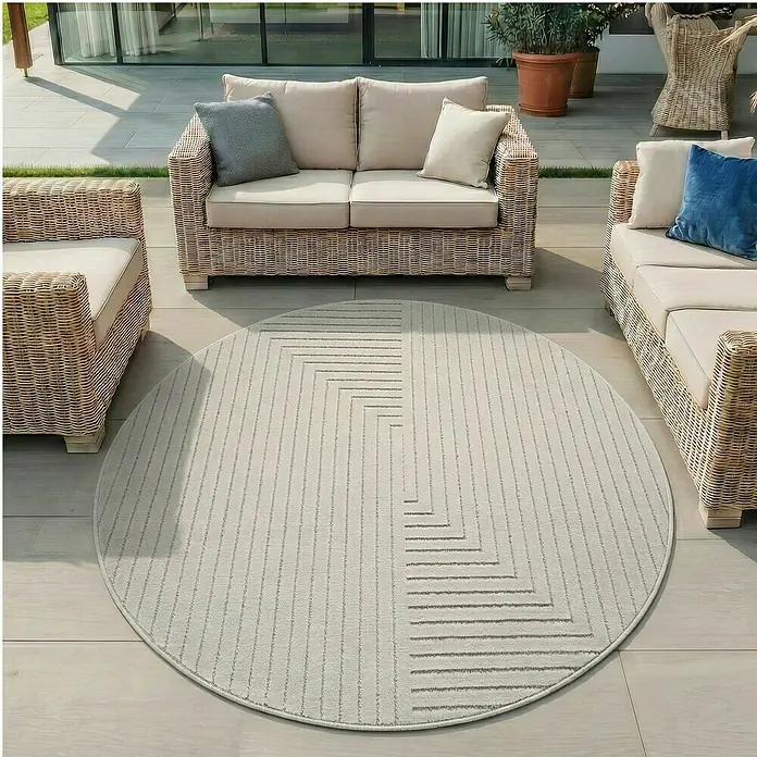 Outdoor-Teppich Nova II - Cream, Durchmesser: 80 cm, 100 % Polypropylen - Ein runder, heller Outdoor-Teppich mit grauem geometrischem Muster auf einer Terrasse mit Korbmöbeln.