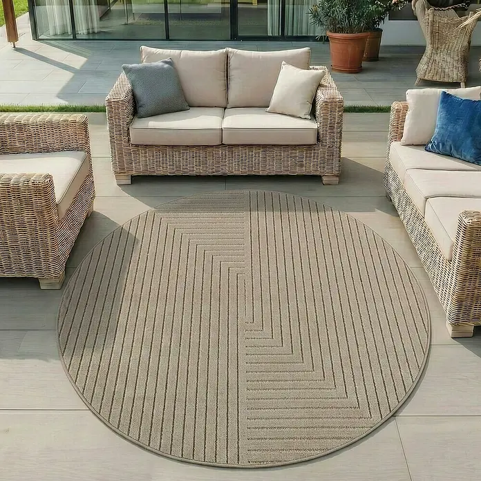 Outdoor-Teppich Nova II - Beige, Durchmesser: 80 cm, 100 % Polypropylen - Runder beiger Outdoor-Teppich mit gestreiftem und geometrischem Muster, auf einer Terrasse unter Rattanmöbeln platziert.