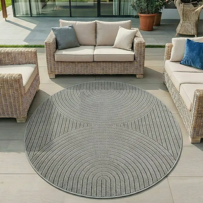 Outdoor-Teppich Nova I - Silver, Durchmesser: 80 cm, 100 % Polypropylen - Runder grauer Outdoor-Teppich mit abstrakt gestreiften Mustern auf einer Terrasse mit Korbmöbeln.