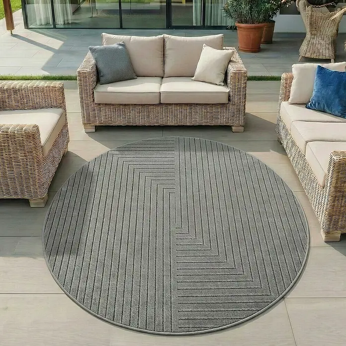 Outdoor-Teppich Nova II - Silver, Durchmesser: 80 cm, 100 % Polypropylen - Runder grauer Outdoor-Teppich mit modernem gestreiftem Geometriemuster auf einer Terrasse unter Korbmöbeln.