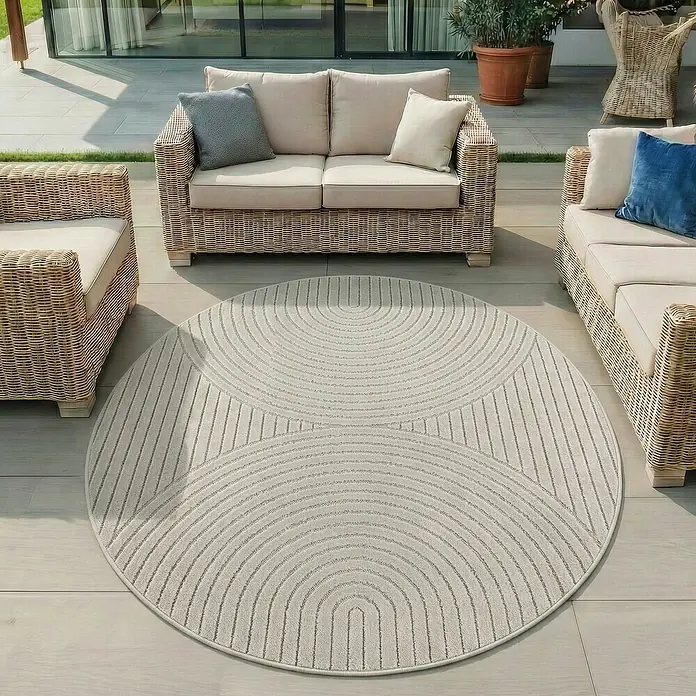 Outdoor-Teppich Nova I - Cream, Durchmesser: 80 cm, 100 % Polypropylen - Heller runder Outdoor-Teppich mit geometrischem Bogenmuster, auf einer Terrasse unter Korbmöbeln.