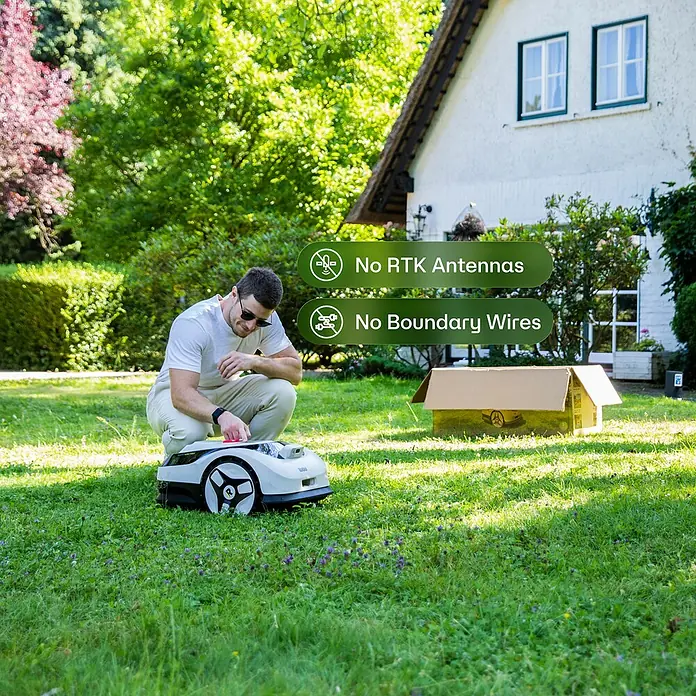 RoboUp Mähroboter Raccoon 2 SE - 600 m², Schnittbreite: 20 cm, Kamera-gestützte Navigation - Mann stellt einen weiß-schwarzen Mähroboter auf grünem Rasen ein. Modernes Design mit markanten schwarzen Rädern.