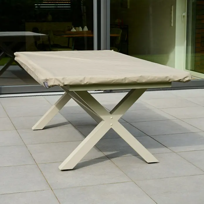 Siena Garden Gartentisch-Schutzhülle PLUS - L x B x H: 180 x 110 x 15 cm, Polyester, TPU laminiert, Beige - Hellbeiger Schutzbezug auf einem Gartentisch mit cremefarbenem X-Gestell auf einer Terrasse.