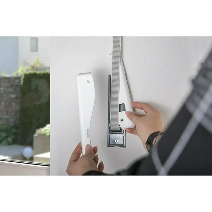 Schellenberg Abdeckplatte Duo210 x 64 x 9 mm, Lochabstand: 160 mm, Weiß - Eine Person montiert ein weisses Rollo mit grauem Gurtband an einer Wandhalterung. Das Rollo-System wird in einem modernen Interieur installiert.