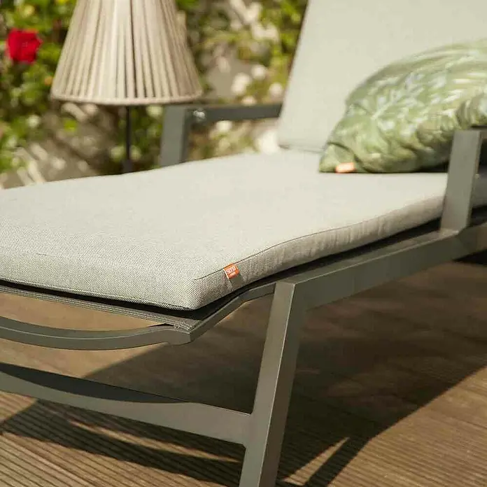 Gartenliege Valencia - B x T x H: 70 x 154 x 102 cm, Aluminium, Polypropylen, Anthrazit - Eine Outdoor-Liege mit dunkelgrauem Rahmen und hellgrauem Kissen, akzentuiert durch ein grünes Kissen, auf einer Holzterrasse.
