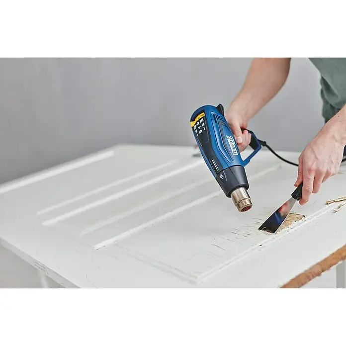 Rapid Pistola de aire caliente R2200 - 2.200 W, Rango de temperaturas: 60 °C - 650 °C - Una pistola de calor Rapid azul utilizada para quitar pintura vieja de una puerta de madera blanca con un rascador.