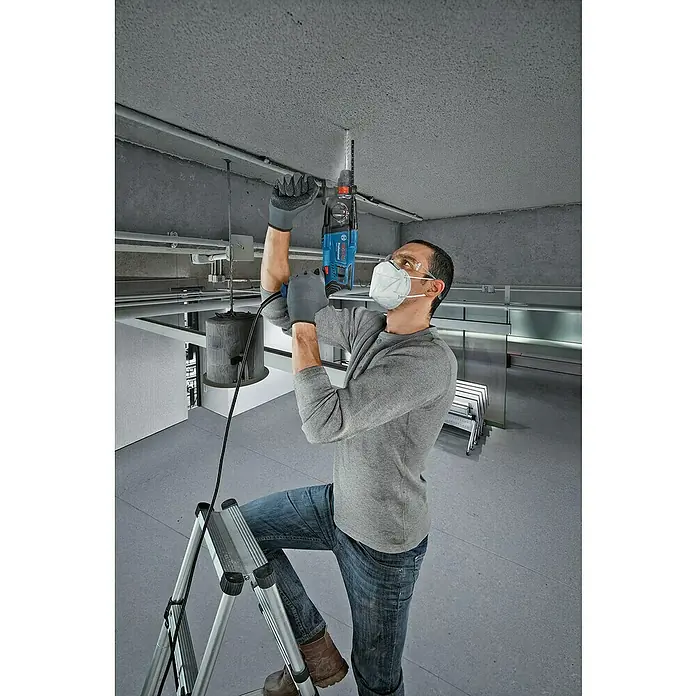 Bosch Professional Bohrhammer GBH 2-21 - 720 W, 2 J, SDS-Plus-Aufnahme - Mann bohrt mit blau-schwarzem Bosch Bohrhammer in Betondecke, auf Leiter stehend.