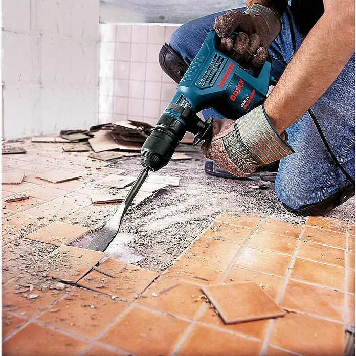 Bosch Professional Abbruchhammer GSH 3 - 650 W, 2,6 J, SDS-Plus-Aufnahme - Blauer Bosch Abbruchhammer entfernt Terrakotta-Bodenfliesen, bedient von einer Person mit Handschuhen.