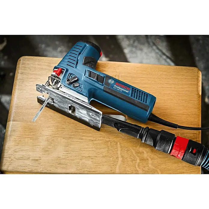 Bosch Professional Elektro-Stichsäge GST 160 CE - 800 W, 800 /min - 3.000 /min - Blaue Bosch Professional GST 160 CE Stichsäge mit eingesetztem Sägeblatt, an Staubabsaugung angeschlossen, auf Holz liegend.