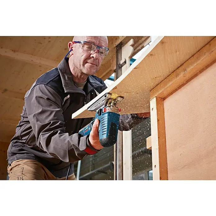 Bosch Professional Elektro-Stichsäge GST 160 CE - 800 W, 800 /min - 3.000 /min - Mann schneidet Holz mit einer blau-schwarzen Bosch Stichsäge. Späne fliegen, er trägt Schutzbrille.