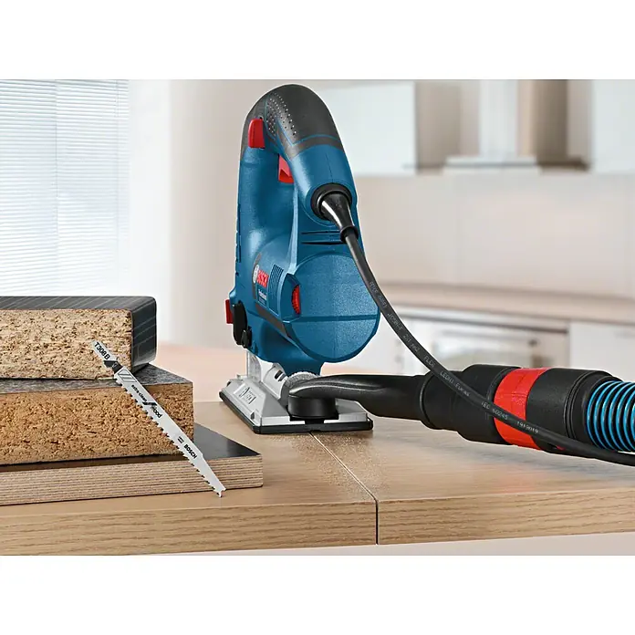 Bosch Professional Elektro-Stichsäge GST 160 CE - 800 W, 800 /min - 3.000 /min - Blaue Bosch Stichsäge mit Staubabsaugung auf Holzoberfläche, neben T308B "extra-clean" Holzsägeblatt und Holzplatten.