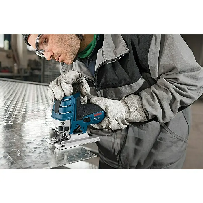 Bosch Professional Elektro-Stichsäge GST 150 CE - 500 /min - 3.100 /min - Ein Mann mit Schutzbrille und Handschuhen benutzt eine blaue Bosch Stichsäge, um ein Metallblech zu schneiden.