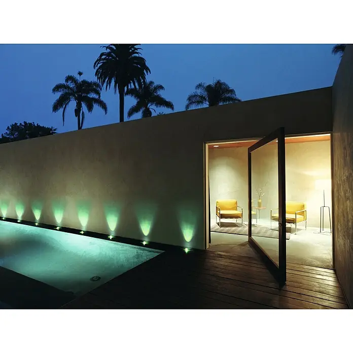 Ledvance LED-Lichterkette Endura Dot - Außen, 9,25 m, Lichtfarbe: Warmweiß, Anzahl Leuchtmittel: 9 Stk. - Moderner Außenbereich mit Pool, beleuchteter Wand und Palmen, neben einem warmen Innenwohnbereich mit gelben Stühlen.