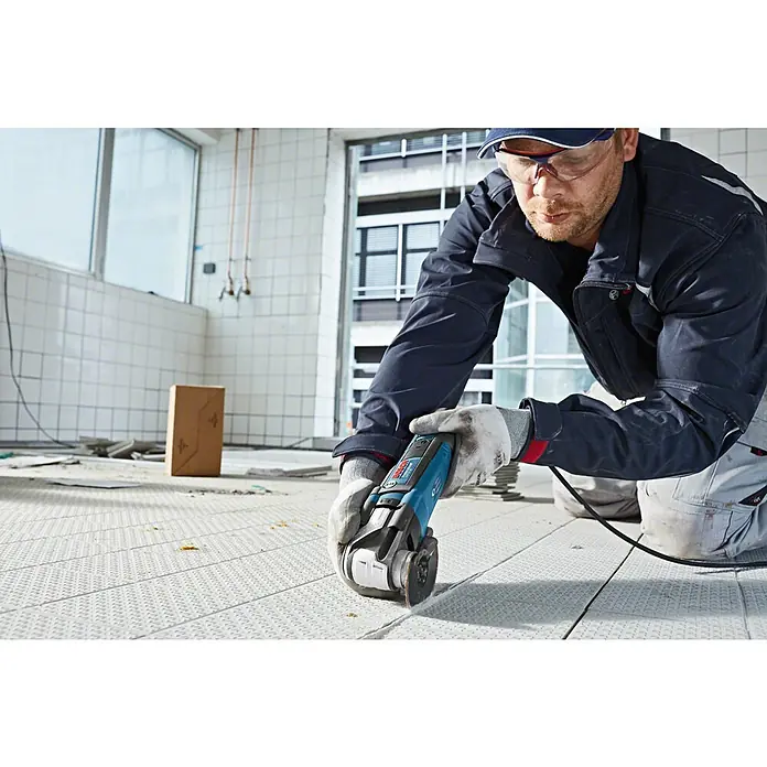 Bosch Professional Elektro-Multifunktionswerkzeug GOP 55-36 - 550 W, Oszillationswinkel: 1,8 ° - Ein Arbeiter kniet und schneidet mit einem blau-schwarzen Bosch Multifunktionswerkzeug einen hellen Boden.