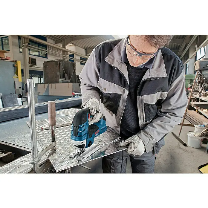 Bosch Professional Elektro-Stichsäge GST 150 CE - 500 /min - 3.100 /min, 150 mm - Person mit Schutzbrille und Handschuhen benutzt eine blau-schwarze Bosch Stichsäge zum Schneiden eines Riffelblechs.