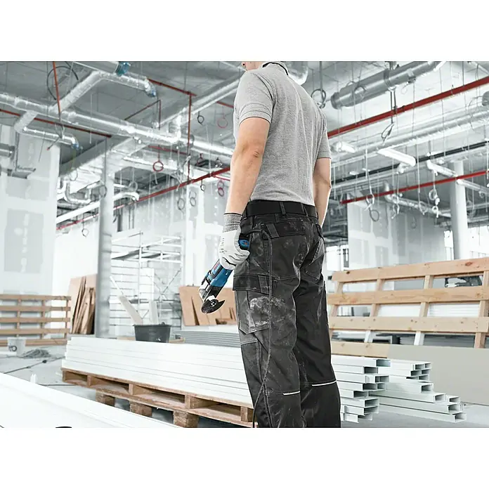 Bosch Professional Elektro-Multifunktionswerkzeug GOP 55-36 - 550 W, Oszillationswinkel: 1,8 ° - Arbeiter hält blau-schwarzes oszillierendes Multifunktionswerkzeug auf einer Baustelle.