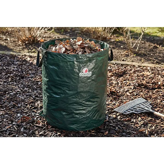 Gardol Gartenabfallsack - 350 l, Höhe: 90 cm, Durchmesser: 70 cm - Grüner Gardol Gartenabfallsack, gefüllt mit trockenem Laub, steht auf Rindenmulch neben einem Rechen im Garten.
